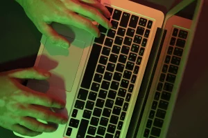 Mains tapant sur un clavier d'ordinateur dans une ambiance sombre avec des reflets verts et rouges, illustrant le cyberharcèlement.