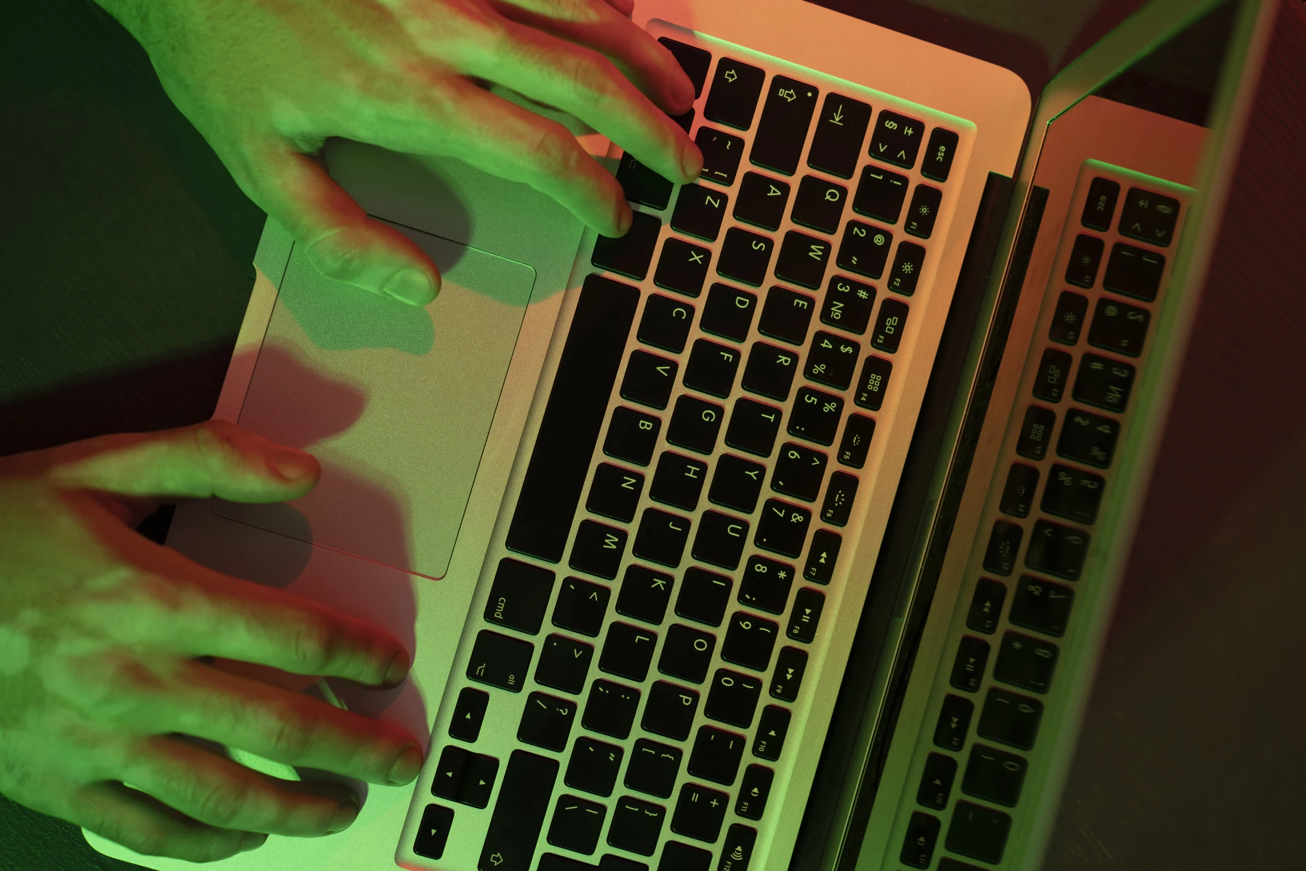 Mains tapant sur un clavier d'ordinateur dans une ambiance sombre avec des reflets verts et rouges, illustrant le cyberharcèlement.