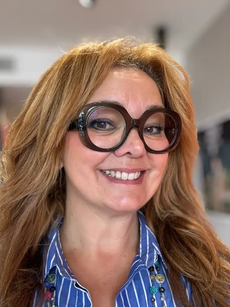 Portrait de Christelle Ramos, référente pédagogique. Elle est souriante avec des lunettes et une chemise bleue à rayures.