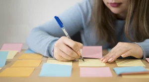 Une jeune femme de face, écrivant sur des post-it colorées afin d'organiser ses idées.
