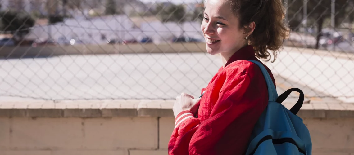 Jeune femme de face, souriante, portant son sac à dos pour sa rentrée scolaire.