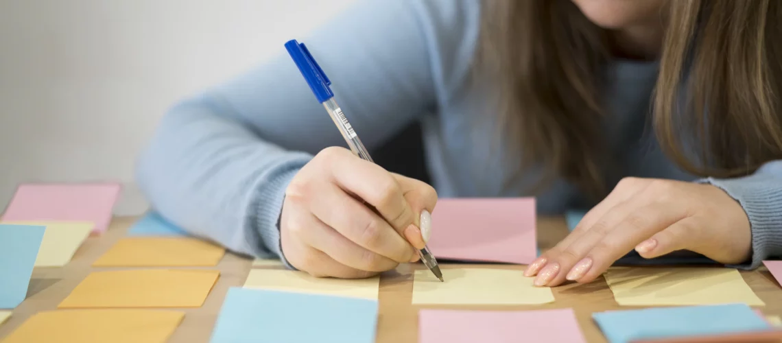 Une jeune femme de face, écrivant sur des post-it colorées afin d'organiser ses idées.