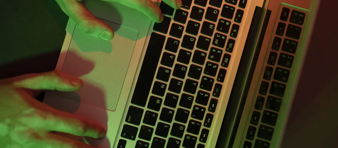 Mains tapant sur un clavier d'ordinateur dans une ambiance sombre avec des reflets verts et rouges, illustrant le cyberharcèlement.
